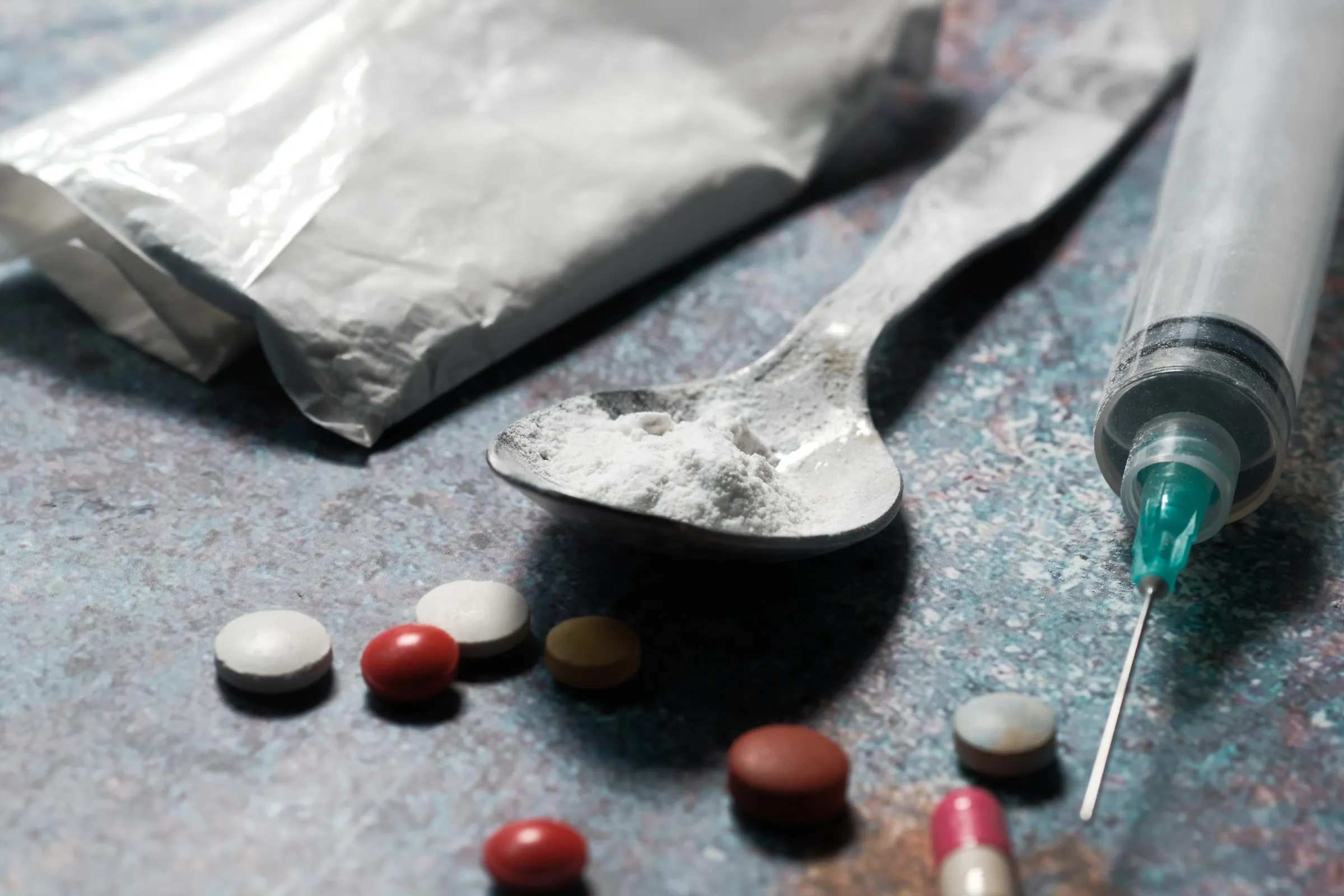 A bag of powder, a spoon, a syringe and pills on a table
